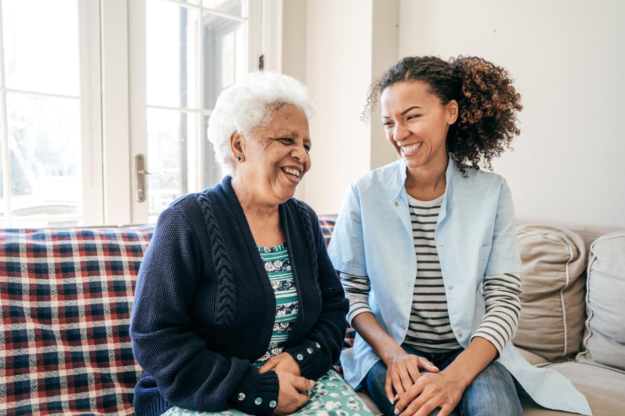 Senior woman sitting on couch with care worker and both are smiling